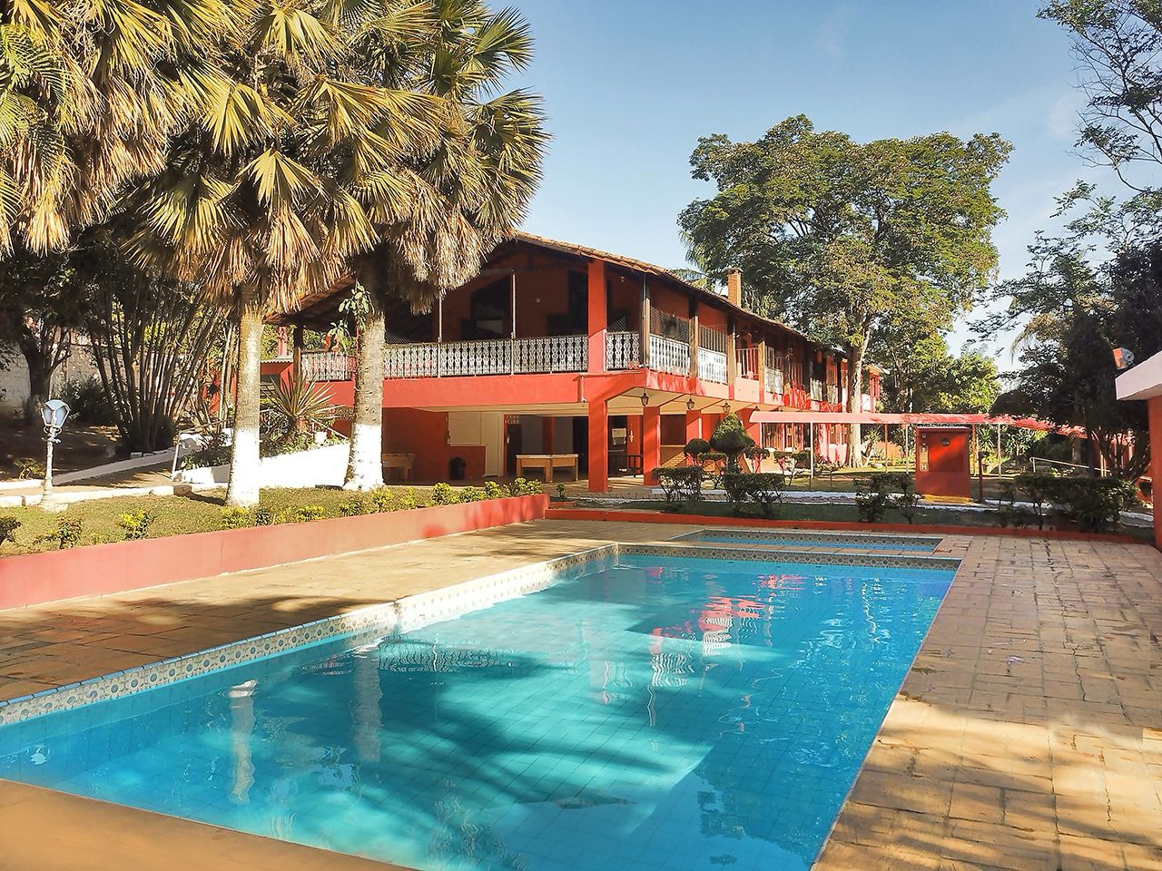 Piscina externa com área verde e prédio de acomodações ao fundo